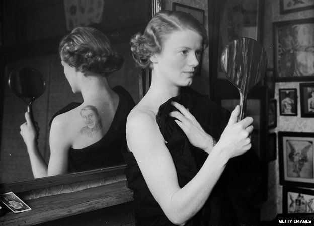 14th November 1936: A film fan uses a mirror to admire the image of film star Gary Gooper she has had tattooed on her back by George Burchett a London tattooist