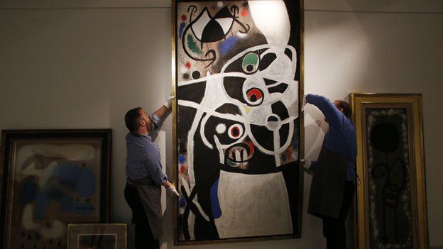 In this 19 December file photo, auction house workers adjust Joan Miro"s 1968 oil painting "Women and Birds" in a room with other works by Miro, at Christie's auction house in central London.