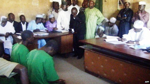 На снимке, сделанном 22 января 2014 г., двое подозреваемых в гомосексуализме в зеленой тюремной форме (слева) сидят перед судьей в Баучи, Нигерия