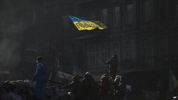 An opposition supporter waves an Ukrainian flag on top of a barricade in a street heading to Kiev"s Independence Square, the epicenter of the country"s current unrest, Ukraine, Thursday, Feb. 6, 2014.