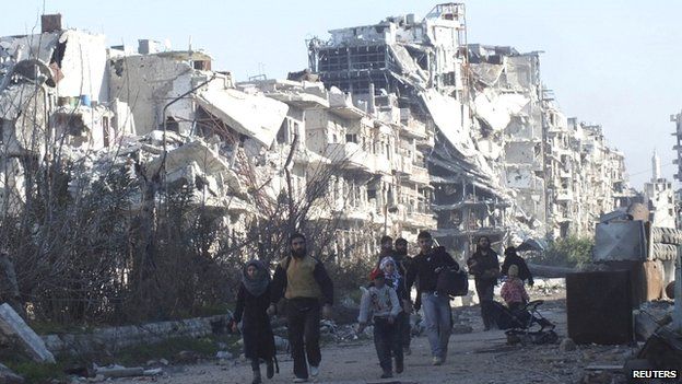 Civilians carry their belongings as they walk towards a meeting point to be evacuated from a besieged area of Homs on 9 February 2014