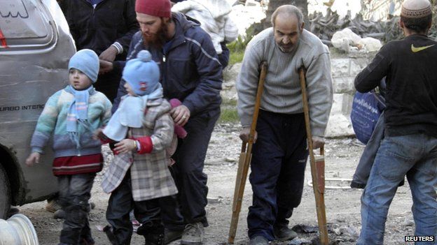 Civilians, including a man with crutches, walk towards a meeting point to be evacuated from Homs on 9 February 2014
