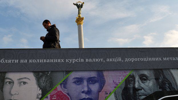 A man stands next to an advertising placard showing British pounds, US dollars and Ukrainian hryvnia banknotes on a warm autumn day in the Ukrainian capital Kiev on 12 November 2012.