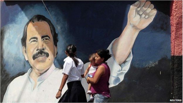 Nicaraguans walk past a Daniel Ortega mural on a wall