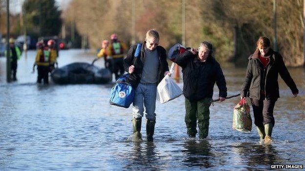 Residents in Chertsey wade through the floods carry their belongings after evacuating their homes