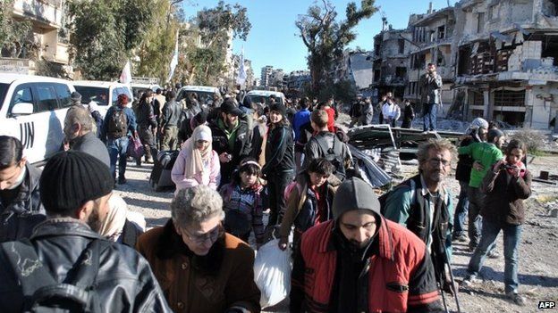 People gather near UN vehicles in a besieged area of the Syrian city of Homs (12 February 2014)