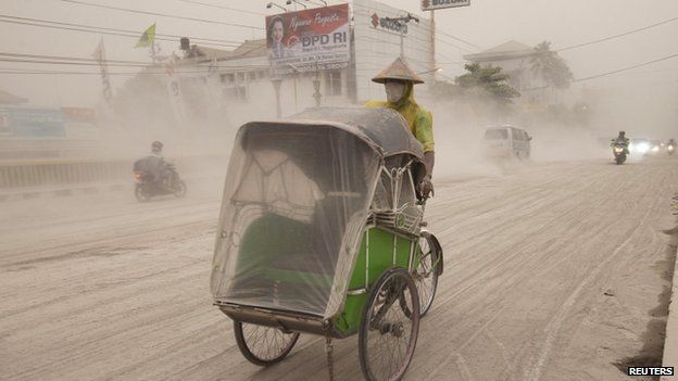 A man wears a mask as he rides a rickshaw on a road covered with ash from Mount Kelud, in Yogyakarta, 14 February 2014