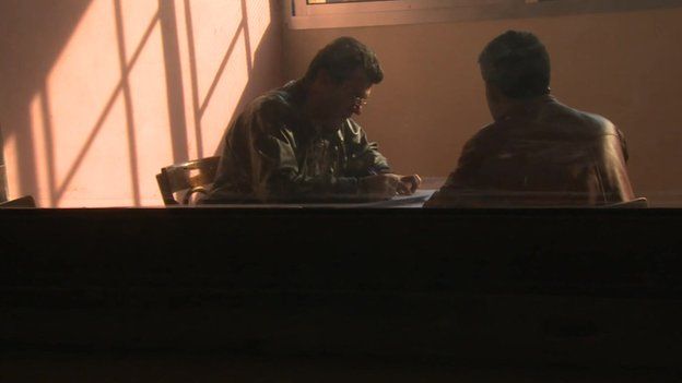 Two men talking inside a classroom at Homs detention centre