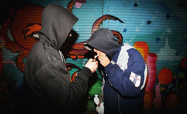 Two youths in hoodies are lighting a cigarette