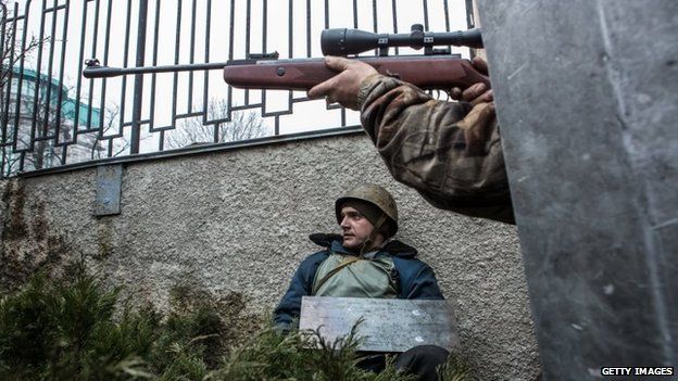 An anti-government protester aims a gun in the direction of suspected sniper fire near the Hotel Ukraine