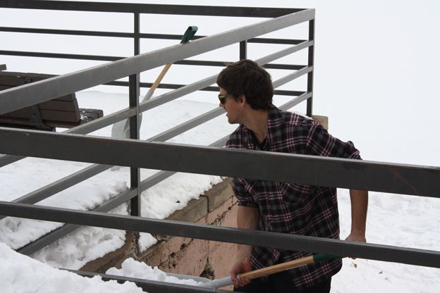 Man shovels snow from under railings