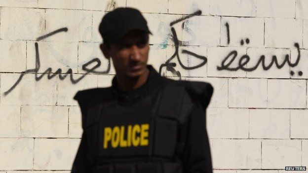 A riot police officer stands guard at the scene of a bomb blast along a wall covered with graffiti around the Al-Azhar University campus in Cairo"s Nasr City district December 26, 2013. The bomb blast hit the bus on Thursday, injuring four people, a spokesman for Egypt's interior ministry told Reuters, two days after a car bomb killed 16 in the Nile Delta. That graffiti says, "Down with military rule."