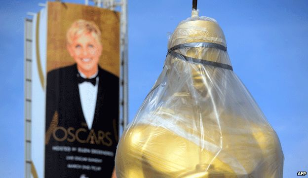 Giant Oscar statue is winched into place in front of a billboard of the host Ellen DeGeneres