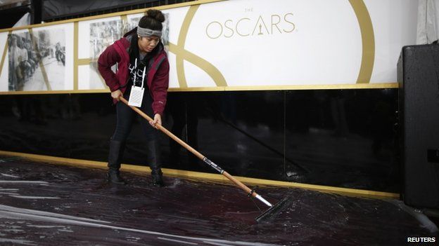 Worker sweeps water from the Oscars carpet outside Dolby Theater