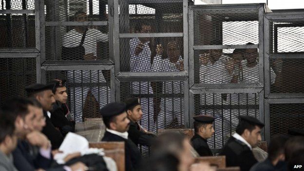 Al-Jazeera journalist Peter Greste (c) and his colleagues inside the defendants cage