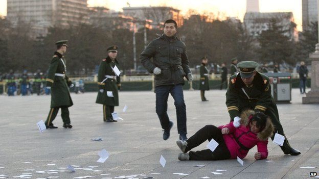 A petitioner is pushed on the ground by a paramilitary policeman after she ran into a cordoned off area near a national flag pole on Tiananmen Square and threw up flyers to protest her case of injustice during a national flag raising ceremony early in the morning before the opening session of the annual National People's Congress at the nearby Great Hall of the People in Beijing, China, 5 March 2014