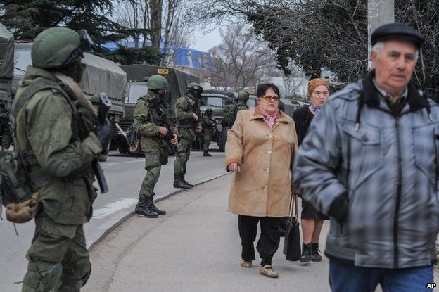 Troops in unmarked uniforms stand guard in Balaklava as people walk in a street, on the outskirts of Sevastopol, Ukraine, Saturday, March 1, 2014.