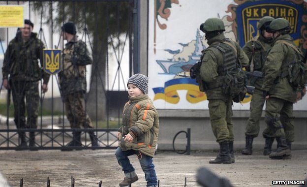 A boy passes by Russian forces blocking access to the base of the 36th detached brigade of the Ukrainian Navy's coastal guards, as Ukrainian soldiers stand guard behind the entrance gate, not far from the village of Perevalne, near Simferopol, on March 5, 2014.