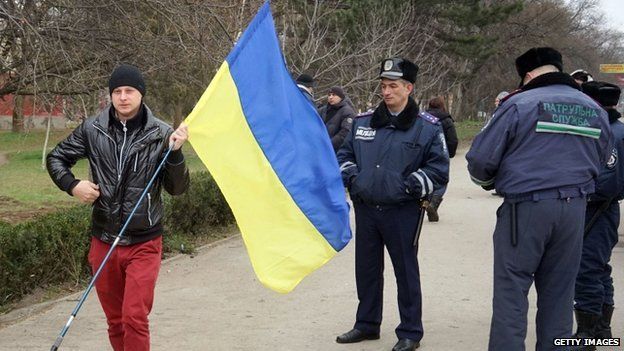 Police officers stand by as a pro-Ukrainian supporter holding a Ukrainian flag parades in Simferopol
