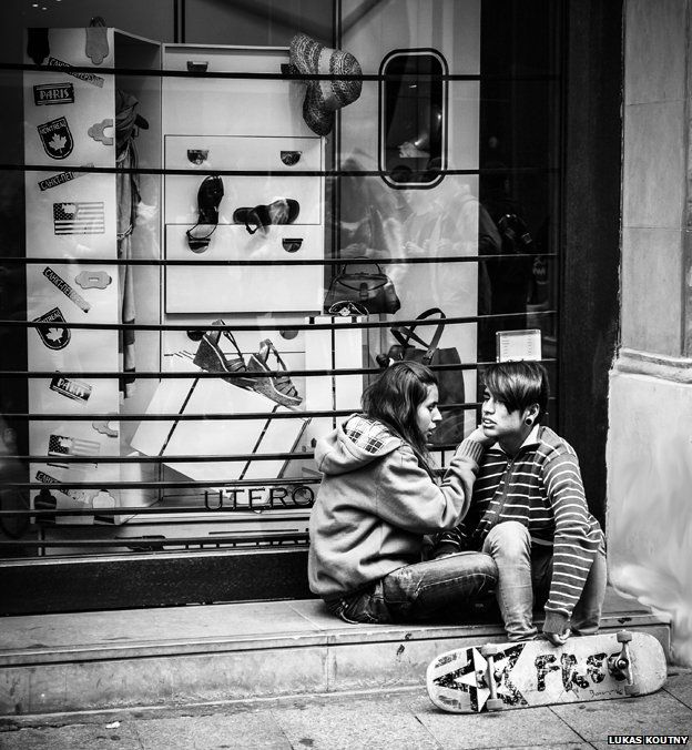 A couple sits on a step in front of a shop