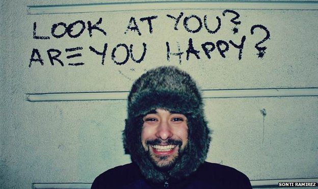 A man smiles under graffiti saying 'Are you happy?'