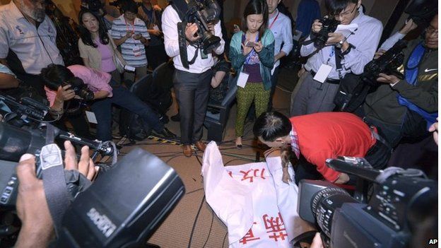 An official takes away a banner reading (in Chinese) "We are against the Malaysian government for hiding the truth and delaying the rescue. Release our families unconditionally!"