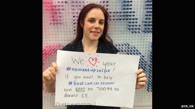 A woman holding a sign asking for donations for Cancer Research