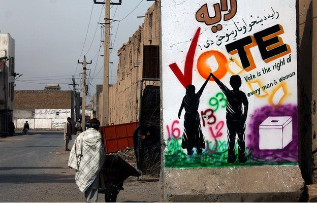 An Afghan pedestrian walks past a wall decorated with an election mural in Kandahar