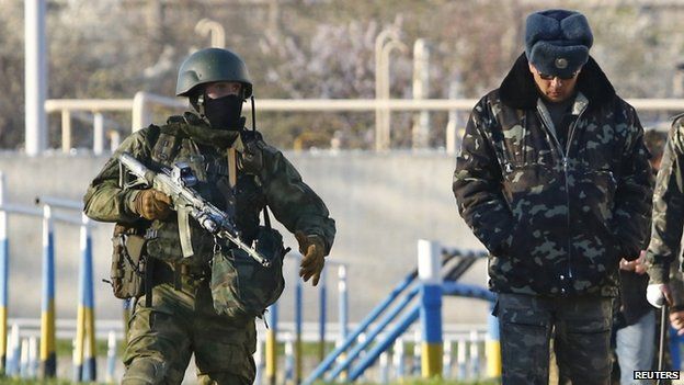 An armed Russian soldier (left) guards a Ukrainian officer at Belbek. Photo: 22 March 2014