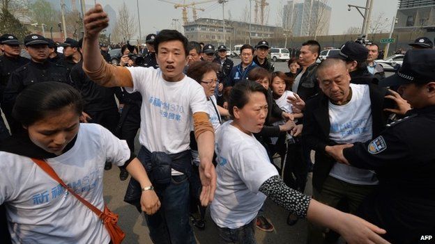 Grieving Chinese relatives of passengers on missing Malaysia Airlines flight MH370 try to remove a police barricade blocking journalists as they gather to protest outside the Malaysian embassy in Beijing on March 25, 2014