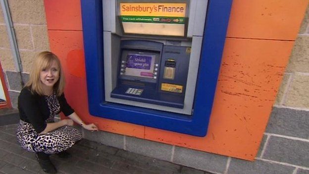 BBC reporter measuring how low the cash machine is off the ground