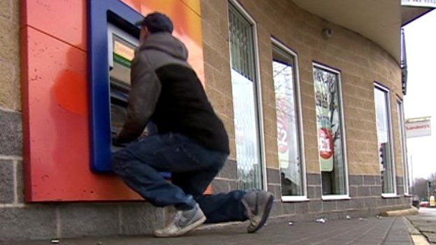 Man kneeling to use a cash machine in Nottingham