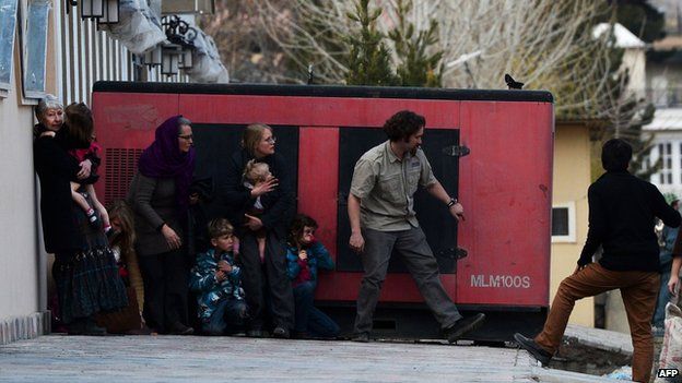 Foreigners take refuge behind a generator after they were evacuated from a guesthouses during an attack by Taliban gunmen (28 March 2014)