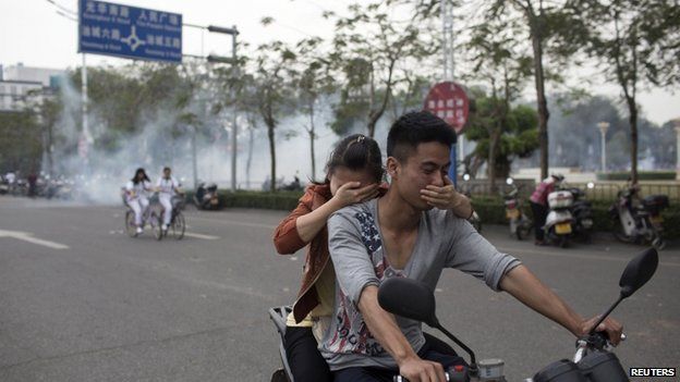 Residents cover their faces as they ride a motorcycle along a street after tear gas was released by police to disperse a protest against a chemical plant project in Maoming, Guangdong province, on 31 March 2014