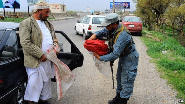 An Afghan policeman searches a bag carrying bread belonging to a resident at the southern entrance to the northwestern city of Herat on April 3, 2014.