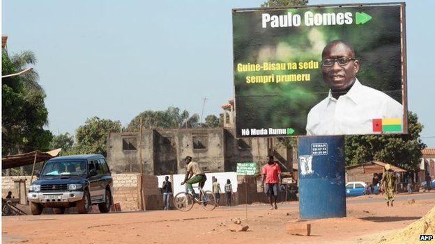 People walk past a campaign poster for presidential candidate Paulo Gomes in a street in Bissau on 11 April