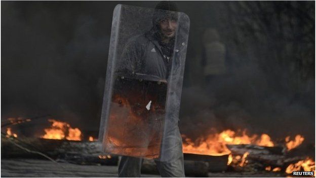A pro-Russian protester holds a shield at a check point, with black smoke from burning tyres rising above, in Sloviansk April 13