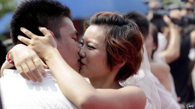 This picture taken on August 13, 2013 shows newly-married couples kissing each other at their wedding ceremony at the Happy Valley theme park in Wuhan in central China's Hubei province, on the Chinese traditional Qixi Festival, known as the 'Chinese Valentine's Day'. The festival dates back over 2,600 years and is a popular and auspicious wedding date for Chinese couples.