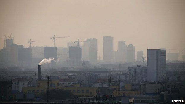 Smoke rises from a chimney among houses as new high-rise residential buildings are seen under construction on a hazy day in Tangshan, Hebei province, on 18 February 2014