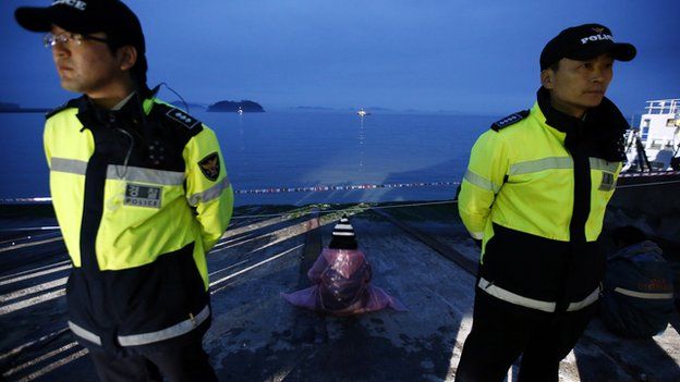 A family member of missing passengers (C) watches the site of the accident, as police officers stand guard at a port in Jindo on 18 April 2014.