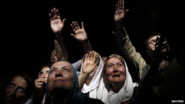 Worshippers react to a beam of sunlight filtering from the ceiling inside the Church of the Holy Sepulcre (19 April 2014)