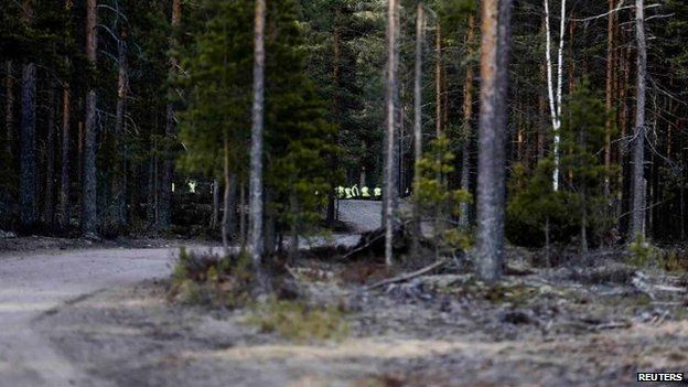 Rescuers are seen through the trees at the Jamijarvi airport site, 20 April