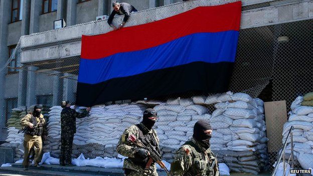 Pro-Russian armed men walk past activists hanging up a 'Donetsk Republic' flag outside the mayor's office in Slaviansk on 12 April 2014