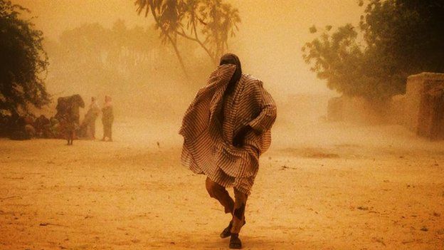 A man from Nigeria in Niger covers his face as he walks through a sandstorm