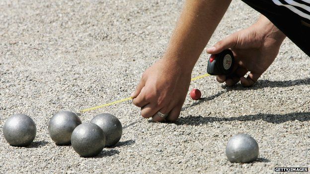 A petanque player measures the distance from a boule to the jack