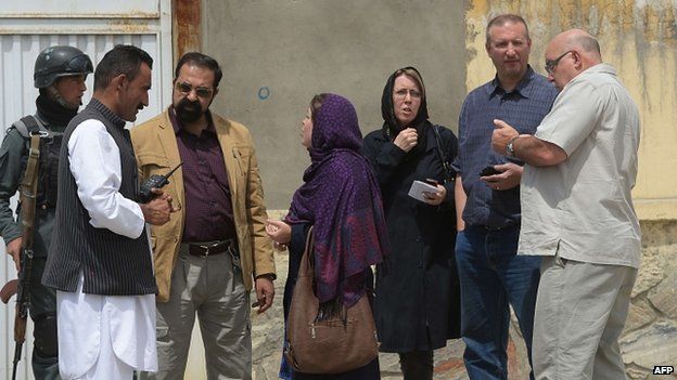 Foreign nationals talk with Afghan security personnel at the gate of the Cure hospital
