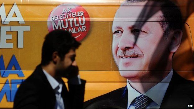 A Turkish man talks on the phone as he walks in front of a poster displaying a portrait of Turkish prime minister Recep Tayyip Erdogan i