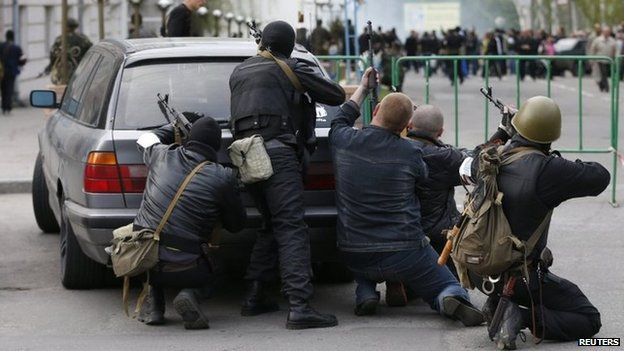 Pro-Russia armed men take cover behind a car near the headquarters of the local police in Luhansk (29 April 2014)