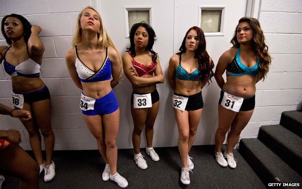 Women in dance attire stand against a wall