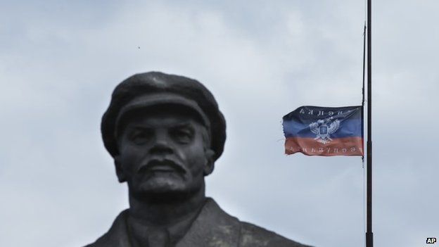 A Donetsk Republic flag on top of an administration building next to the monument of former Soviet leader Vladimir Lenin in the centre of Sloviansk